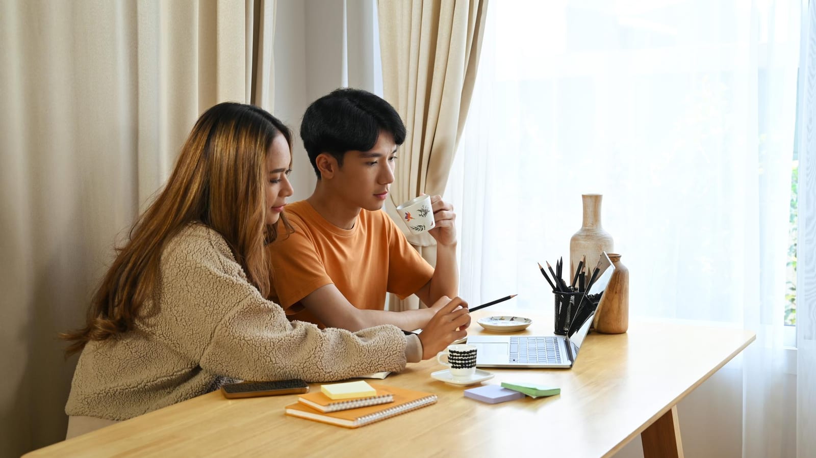 自宅の机でノートパソコンを見ながら書類を確認する夫婦
